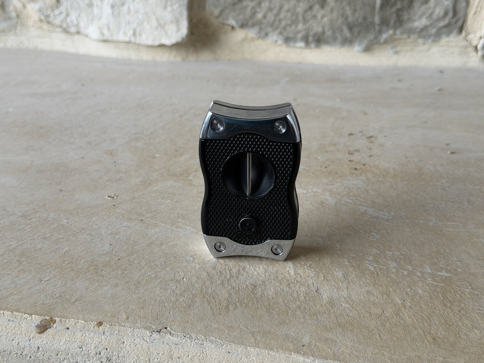 Colibri SV-Cut cutter closed, V-cut side facing, black knurled body with chrome ends on a stone hearth