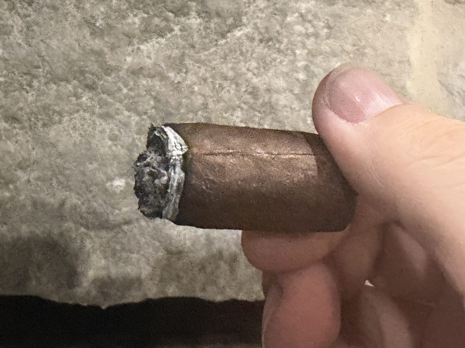 LecheBurra in the final third after dark, band off, with ash forming on the short remaining cigar