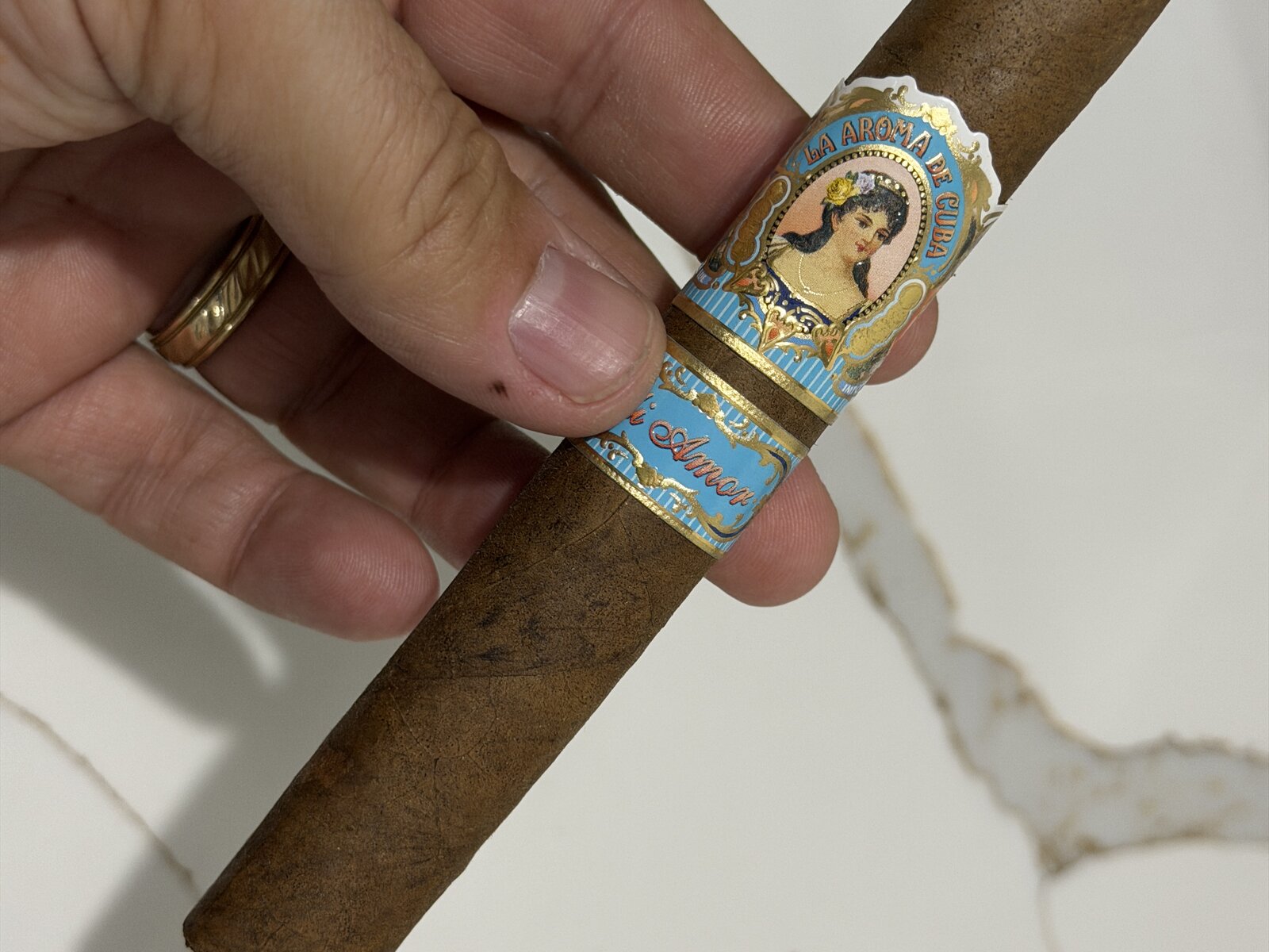 La Aroma de Cuba Mi Amor Magnifico held in hand, box-pressed medium-brown wrapper with the light-blue La Aroma de Cuba señorita primary band and a light-blue and gold Mi Amor secondary band