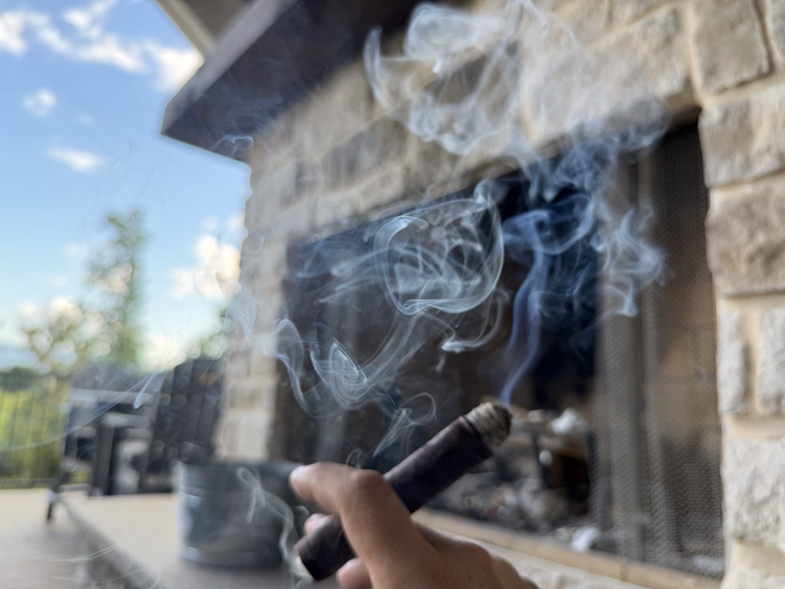 Liga Privada No. 9 Toro pouring thick smoke that hangs in the air over a back deck with a stone outdoor fireplace behind it