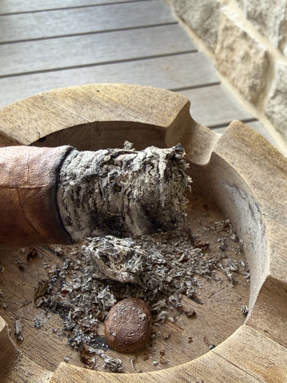 Wonky flaky ash from the Flor de las Antillas knocked into a round wooden ashtray, cigar foot resting on the rim