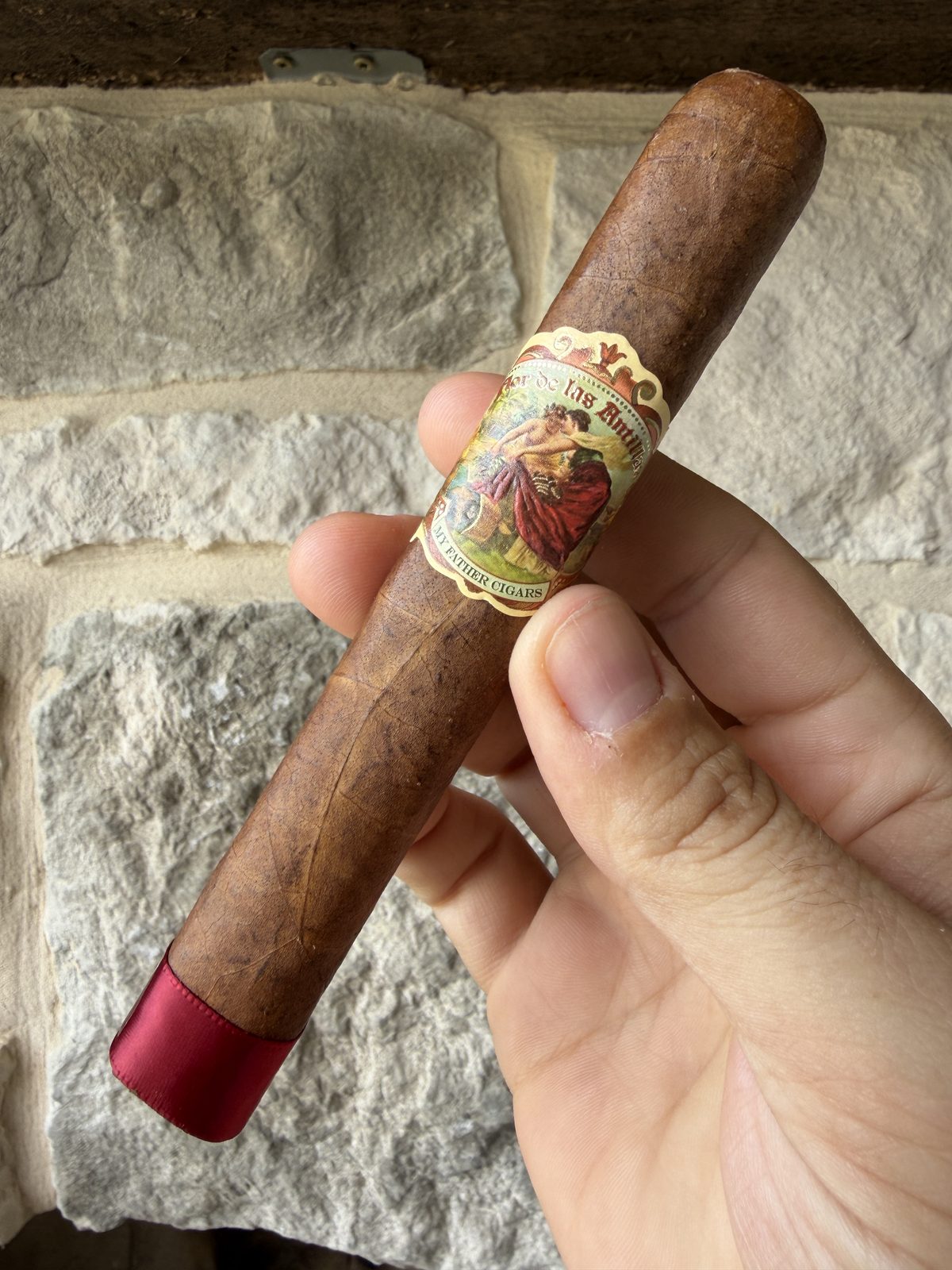 My Father Flor de las Antillas Toro held in hand before lighting, box-pressed medium-brown wrapper, ornate band, red foot ribbon still on the foot