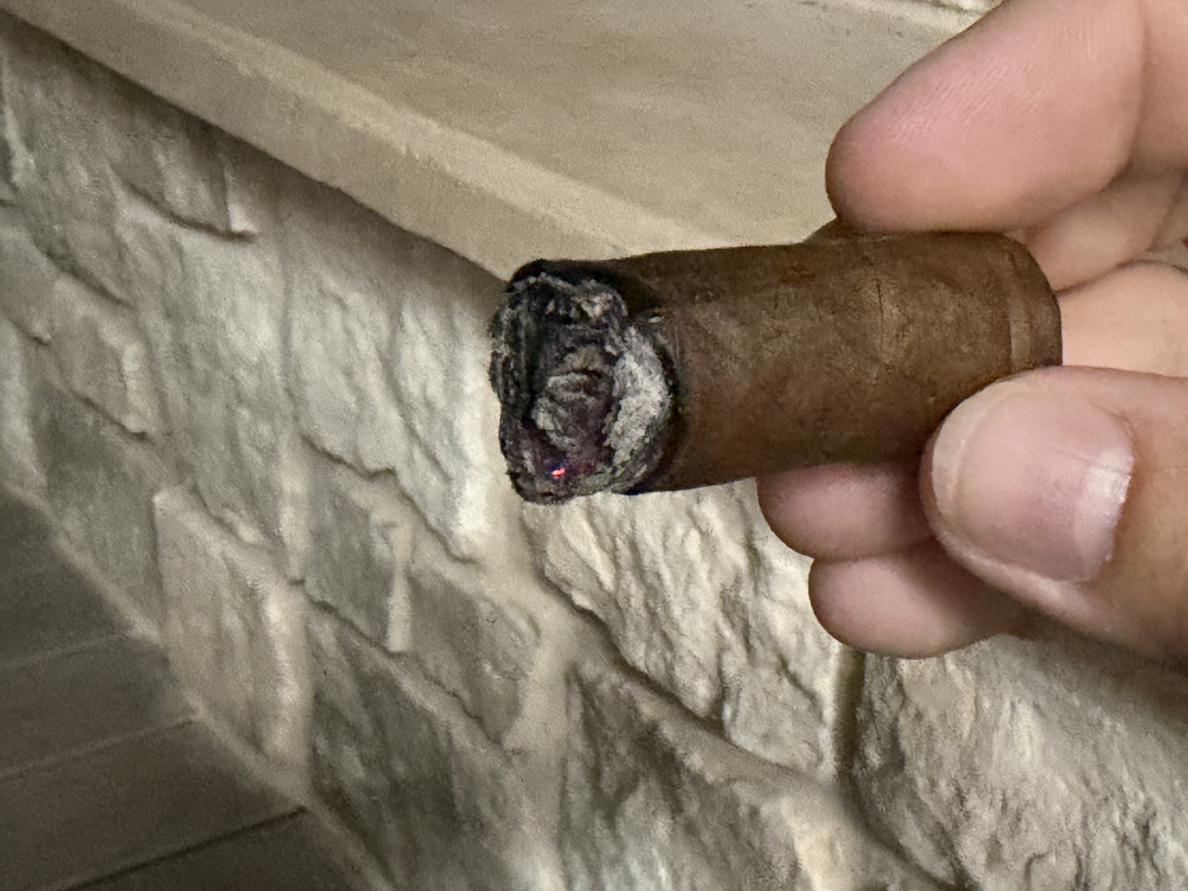 Nub of the La Promesa held in front of a stone fireplace hearth with the ash knocked off, showing a slightly hollow cherry