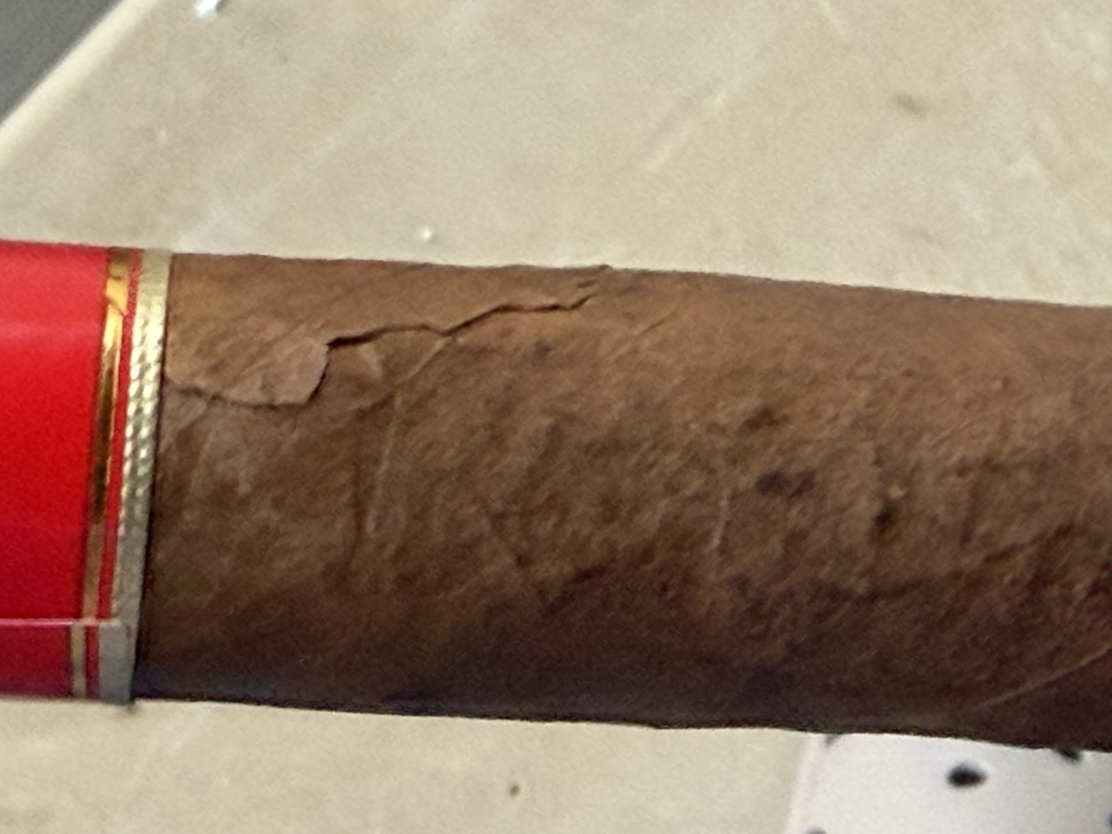 Close-up of cracks in the La Historia Silk wrapper, one running from the edge of the red secondary band and others spidering across the leaf