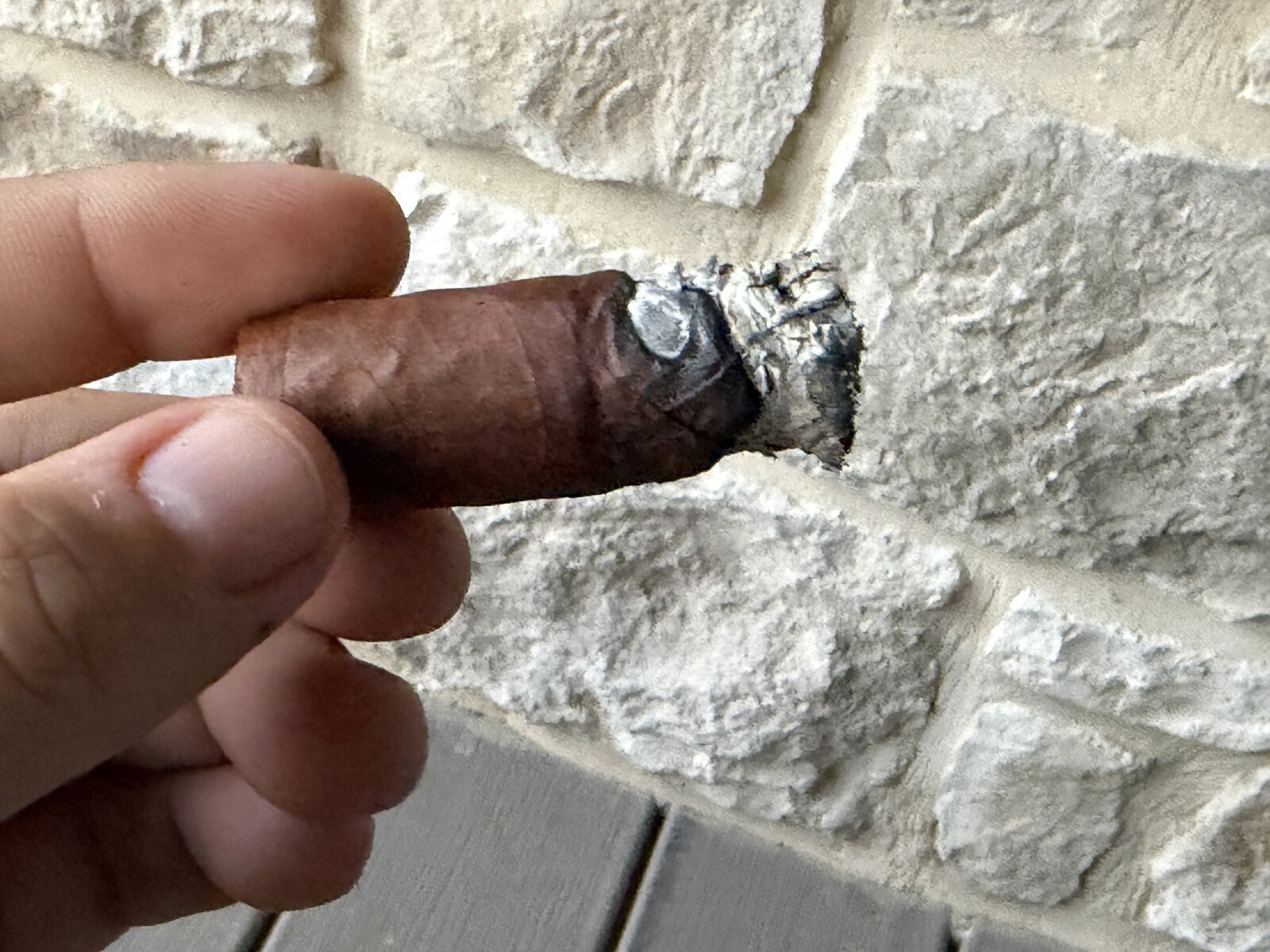Short nub of the Punch Reserve Collection Robusto held against the stone wall, ash still on the foot