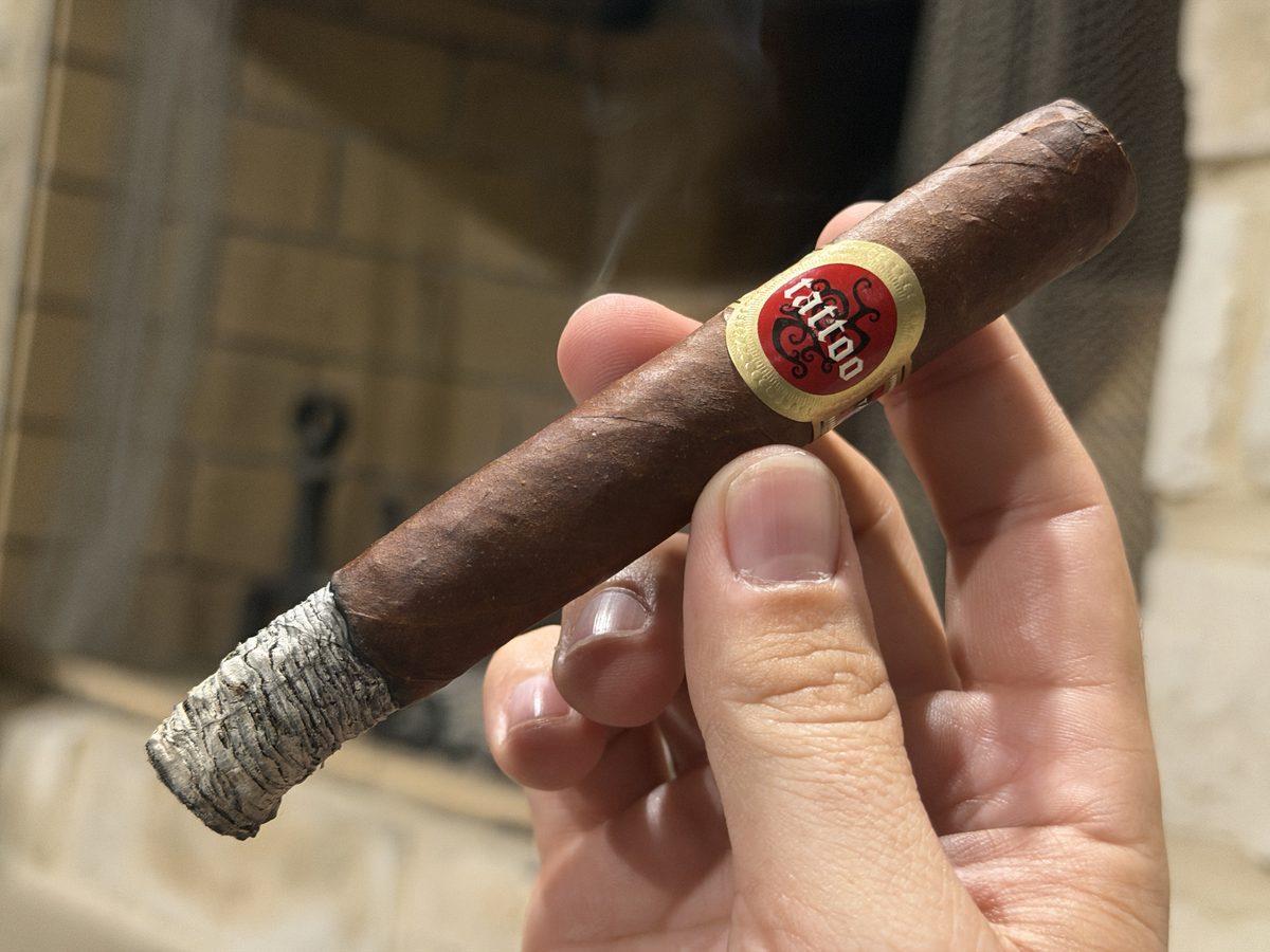 Tatuaje Tattoo Universo lit with a long tight grey ash stacked in dimes, held horizontally