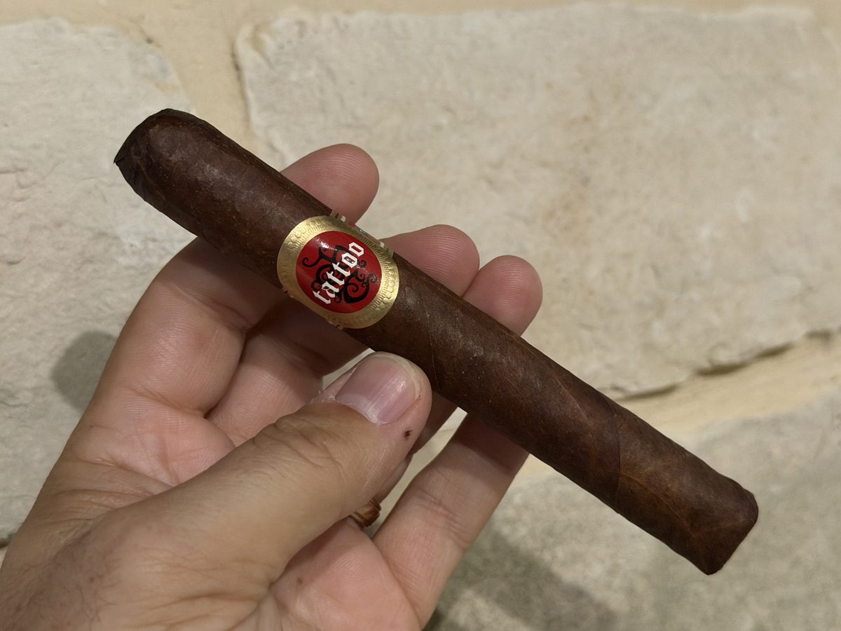 Tatuaje Tattoo Universo held in hand before lighting, dark clean wrapper with the red and gold Tattoo band
