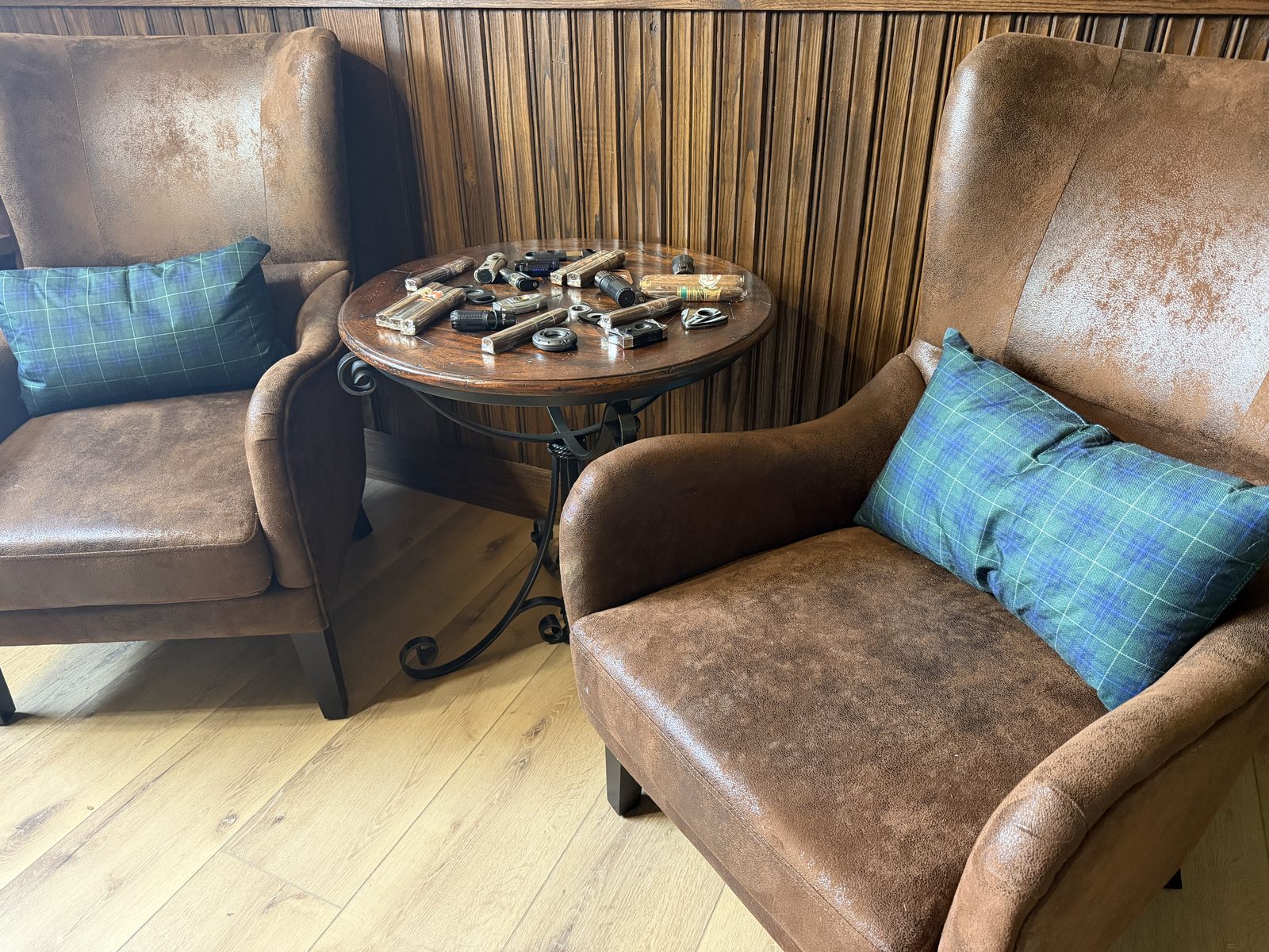 Two leather chairs and a small round table holding cigars and cutters, in a wood-paneled corner