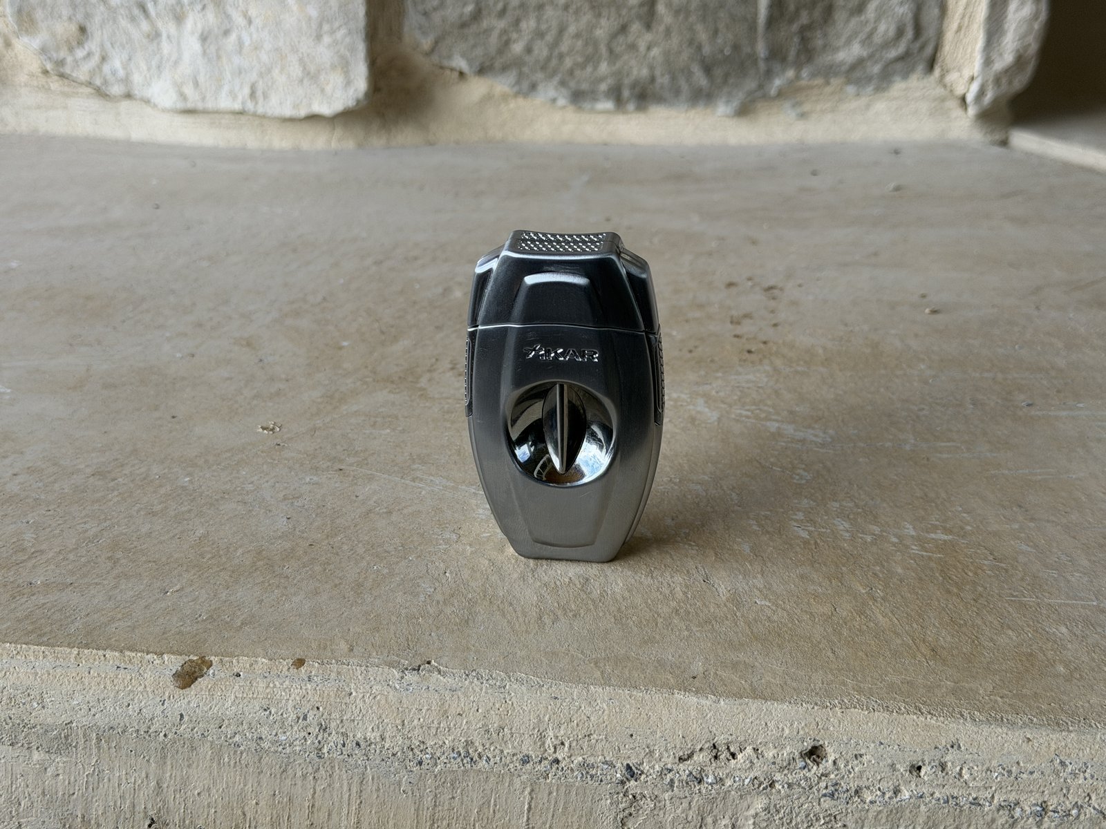 Xikar VX2 V-cut cutter closed, silver body with the polished V-cut bowl, standing on a stone hearth
