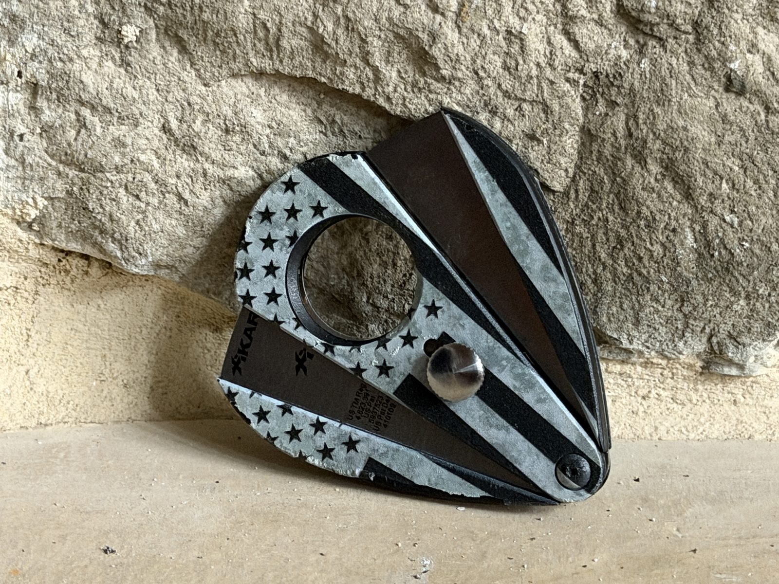 Xikar Xi2 Hero Series cutter leaning against a stone wall showing the teardrop shape and flag graphic